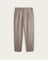 A pair of light taupe pleated trousers shown flat against a warm off-white background.